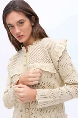 Cardigan de punto color beige con volados en el canesú, mangas largas, calados sutiles y botones forrados del mismo material.