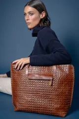 Bolso tipo tote de cuero vacuno con textura de reptil, color marrón. Presenta detalles de pasamanería en los bordes laterales y una borla de flecos de cuero colgante. Cuenta con cierre superior.