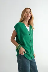 Chaleco de punto color verde, con escote en V y cierre frontal de botones negros. Presenta un diseño holgado con terminaciones acanaladas en el cuello, sisas y ruedo.