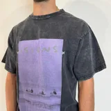 Remera de corte oversize con efecto de lavado ácido en color negro. Presenta un estampado rectangular central en tonos violeta con la palabra 'VISIONS' y una escena de surfistas en el mar.