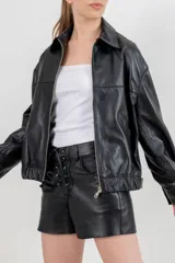 Chaqueta bomber de cuero ovino color marrón oscuro, con cuello clásico, hombros caídos y ajuste elástico en la cintura. Presenta bolsillos con vivos y broches ocultos, y ajustes metálicos en puños y espalda.