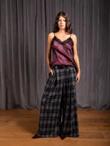 Pantalón tipo palazzo de corte amplio y tiro alto, con diseño de estampado a cuadros tipo tartán en tonos grises y negros. Presenta pinzas frontales, bolsillos laterales y cierre con trabillas para cinturón.