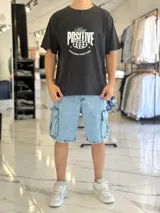 Remera negra con efecto gastado (acid wash), de corte oversize, con estampa frontal en blanco y celeste con la leyenda 'Stay Positive' y diseño gráfico de un globo terráqueo.