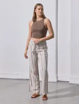 Pantalón largo de lino color beige con rayas verticales marrones. Tiene pretina ancha en punto smock con lazo ajustable, bolsillos verticales delanteros y bolsillos aplicados traseros.