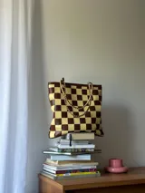 Bolso tipo tote de cuero trenzado a mano con diseño de damero en colores marrón y beige. Cuenta con doble asa trenzada y forro interior.