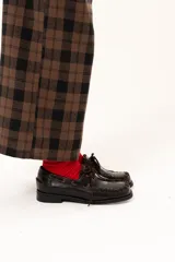 Zapato náutico de cuero color chocolate con horma cuadrada. Presenta detalles de pasamanería en cuero descarne que recorren el frente y los laterales, cordones frontales y suela plana con pequeño taco.