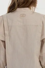 Camisa de algodón a rayas color beige y blanco, con cuello mao, volados en los hombros, mangas abullonadas y nudo frontal en el dobladillo.