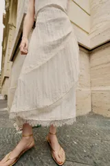 Vestido midi lencero de color blanco, confeccionado en tejido con efecto arrugado. Cuenta con escote recto, tirantes finos ajustables, diseño cruzado con cinturón fino para anudar y detalles de encaje en los acabados de la falda.