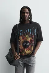 Camiseta de punto negro con efecto lavado, corte relaxed fit y cuello redondo. Presenta un estampado frontal con tipografía gótica en azul y una imagen circular que simula un iris en tonos rojizos y amarillos.