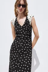 Vestido midi de lunares, color negro con lunares blancos, escote en V y mangas sisa con hombreras. Presenta frunces laterales en la cintura y cierre en la espalda con cremallera oculta.