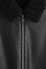 Campera de tejido revestido con acabado efecto cuero, cuello de solapa con forro de sherpa, cierre frontal con cremallera metálica y bolsillos laterales con cierre.