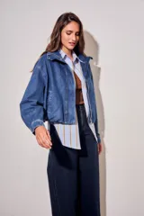 Campera bomber de jean con corte oversize, cierre frontal y cuello alto con botones a presión. Presenta mangas amplias y puños ajustados.