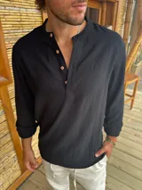 Camisa de lino negra con cuello mao y cierre frontal parcial con botones de madera. Presenta mangas largas con puños arremangados y un corte holgado.