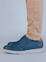 Zapato de estilo casual tipo derby en color azul marino, confeccionado en cuero con detalles de perforaciones decorativas tipo brogue. Cuenta con cordones al tono, detalle en cuero color suela en el talón y suela de goma flexible color gris claro con tecnología de amortiguación.