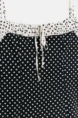 Vestido corto entallado con estampado de lunares, tirantes finos ajustables y escote redondo con detalle de frunces y lazada frontal. Presenta un diseño combinado con contraste de colores en la parte superior y cierre de cremallera oculta en la espalda.