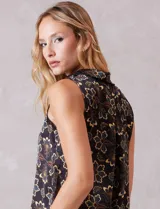 Conjunto de dos piezas compuesto por una blusa sin mangas con cuello solapa y escote en V con botones frontales, y un pantalón de tiro alto con pierna ancha y bolsillos laterales. Ambas prendas están confeccionadas en satén con un estampado floral sobre fondo oscuro.