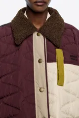Abrigo acolchado de corte recto con diseño patchwork en tonos burdeos, beige y verde oliva. Presenta cuello camisero de pana, cierre frontal con botones de presión, bolsillos de tapeta en el bajo y bolsillos de vivo en el pecho.