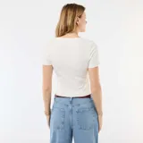 Camiseta blanca de canalé de manga corta, con cuello redondo y terminaciones con volantes sutiles en el cuello y el ruedo.