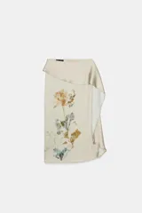 Falda midi de tiro alto, color beige claro satinado, con un diseño asimétrico o drapeado en la cintura. Presenta un estampado botánico de flores prensadas en tonos ocres, azules y verdes en el frente.