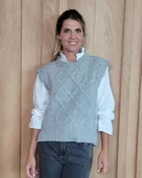 Chaleco de punto gris con diseño de trenzas y rombos en relieve, cuello redondo y terminaciones acanaladas.