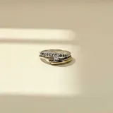 Anillo de diseño cruzado fabricado en plata y oro, con una hilera de circonias engastadas en la parte superior y una piedra central destacada.