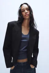 Blazer corto de corte recto con cuello de solapa, manga larga y hombreras. Presenta un diseño minimalista sin botones y forro interior a tono.