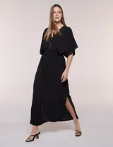 Vestido largo amarillo de corte fluido con escote en V, mangas cortas amplias y apliques de tachas en el escote y puños. Posee cintura elastizada fruncida y falda larga con tajos laterales en el ruedo.