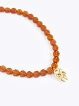 Collar de cuentas de vidrio color ámbar con un charm dorado en forma de llama en el centro. Incluye cadena de extensión y cierre de mosquetón.