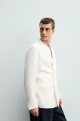 Blazer color crudo de lino y algodón, corte regular, con cuello de solapa de pico, manga larga con puños abotonados, bolsillos de vivo en el pecho y bolsillos de solapa en la cadera, bolsillo interior, aberturas en la espalda y cierre frontal cruzado con botones.