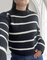 Sweater de punto grueso negro con rayas horizontales blancas, cuello alto y corte holgado.