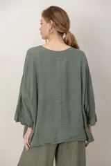 Blusa de lino color verde militar, holgada, de manga 3/4 con volados en los puños, cuello redondo y detalle de alforzas horizontales en el dobladillo.