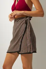 Falda corta tipo pareo con diseño envolvente, confeccionada en tela con estampado de rayas verticales en tonos tierra. Cuenta con un lazo lateral para ajuste y un borde inferior con detalle de costura en contraste.