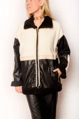 Campera con cuerpo de corderito color beige, mangas y parte inferior de cuero sintético negro con textura tipo cocodrilo. Tiene cuello estilo camisa con solapas de corderito negro, cierre frontal con cremallera y bolsillos laterales.