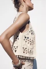 Chaleco abierto de punto color crudo con manga sisa y detalle de conchas en el ruedo.