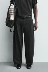 Pantalón chino de corte wide fit confeccionado en tejido de algodón. Presenta pliegues frontales, bolsillos laterales y bolsillos traseros de vivo, con cierre frontal de cremallera y botón.