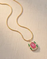 Collar de acero dorado con cadena fina y dije rectangular con gran piedra ovalada fucsia al centro, rodeada por pequeños cristales blancos y verdes.