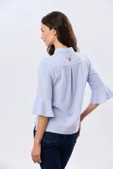 Camisa de lino celeste con cuello clásico, cierre frontal con botones y mangas tres cuartos terminadas en volados.