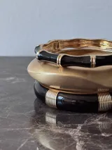 Pulsera rígida tipo brazalete, color negro con detalles dorados.