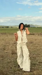 Pantalón de lino color crudo, de corte recto y tiro alto. Presenta apliques verticales de tela plisada a lo largo de las piernas que aportan textura y movimiento, con tajos laterales y bolsillos funcionales.