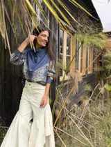 Camisa de corte oversize que combina denim azul en la parte superior y mangas, con un panel inferior de tela estampada con diseño geométrico multicolor. Cuenta con cuello camisero alto y cierre frontal de botones.