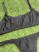 Conjunto de bikini negro con corpiño tipo top y bombacha colaless regulable, confeccionado en tela metalizada.