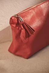 Neceser de cuero marrón con cierre superior y tirador de cuero con flecos.