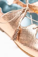 Zapato tipo blucher con diseño híbrido entre blucher y bailarina, confeccionado en piel rosada con textura de reptil. Presenta un acabado orgánico con ondas en el empeine, cierre con cordones con borlas de piel y elástico en la parte trasera para un ajuste óptimo. Cuenta con interior en piel y suela de cuero.