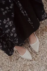 Chatitas destalonadas de cuero charolado color beige con punta fina, taco bajo y detalle de tachas metálicas doradas alrededor del borde.