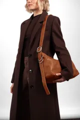 Bandolera de cuero color suela, de diseño descontracturado, con cierre metálico, bolsillo interior y correa ajustable con hebilla y argollas plateadas.