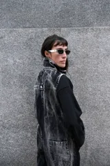 Mono de denim con efecto de lavado ácido en tonos grisáceos y negros. Presenta cierre frontal completo, cuello alto, bolsillos laterales y bordados decorativos en color azul en la parte superior del pecho. De diseño utilitario y corte holgado.