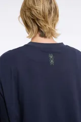 Remera blanca de corte boxy, cuello redondo a la base y mangas cortas. Presenta un pequeño estampado localizado en el centro del pecho que simula un ají en tono rojizo.