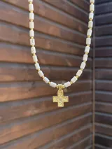 Collar de cuentas cilíndricas blancas con piedras reconstituidas y pequeñas cuentas doradas, con dije colgante de cruz dorada con textura martillada y detalle central.