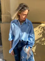 Camisa blanca de corte amplio con mangas tres cuartos abullonadas. Presenta detalles de bordado calado en los hombros y en las mangas, con cierre frontal de botones.