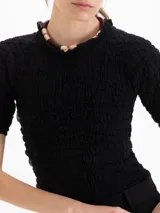 Top Charlotte de algodón y lino color negro, con calce al cuerpo, largo a la primera cadera, frunces en el exterior y escote semi alto con volado, al igual que los puños de las mangas cortas.